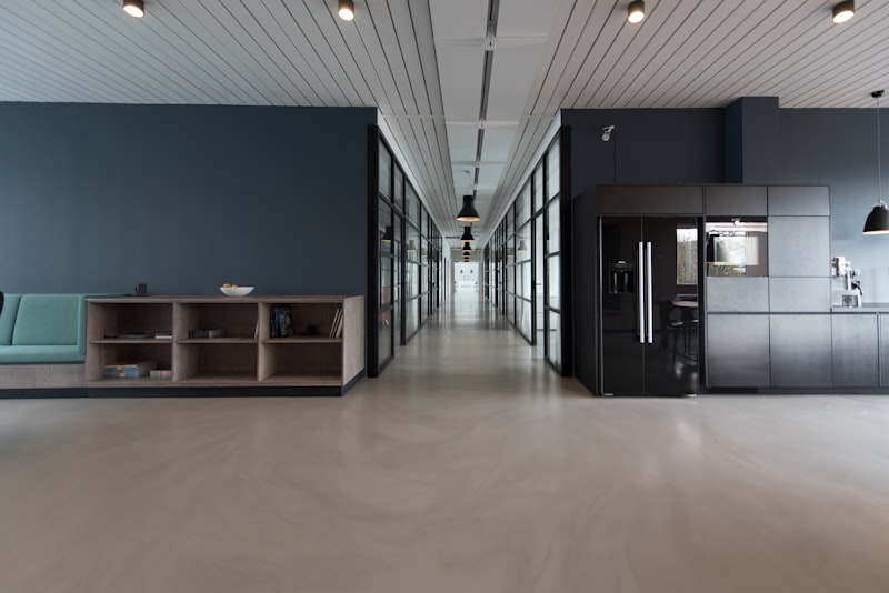 Modern office hallway with glass partitions, wood shelving, and a kitchenette area